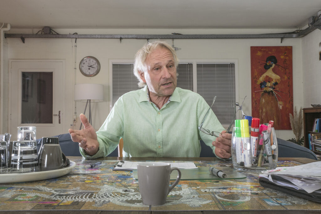 Dit is een afbeelding van Jan Lamers aan zijn tafel in de praktijk.